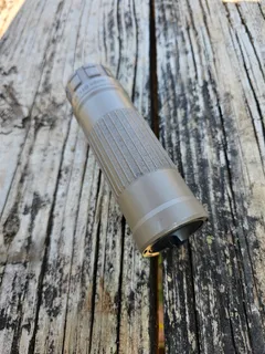 Dead Air Lazarus 6 suppressor in flat dark earth on weathered wood, angled from the muzzle, showing the front cap and the ribbed grip section