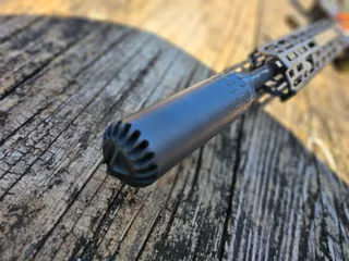 HUXWRX FLOW 556K suppressor mounted on a rifle over weathered wood, angled from the muzzle, showing the vented front cap